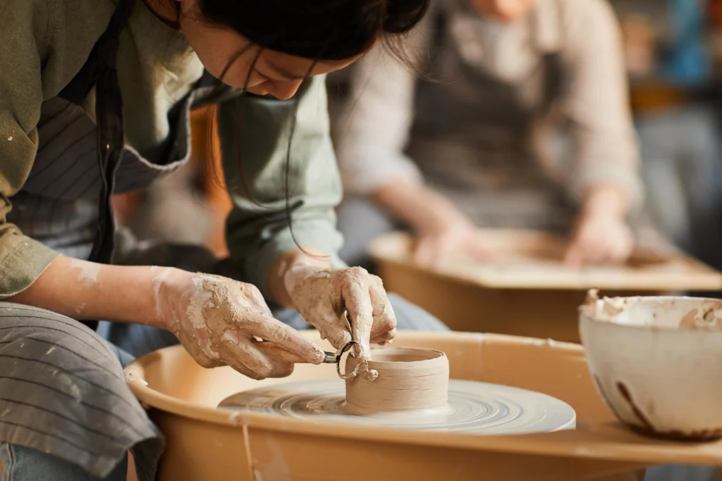 Close-up of a person crafting pottery on a spinning wheel, shaping clay with focused attention.