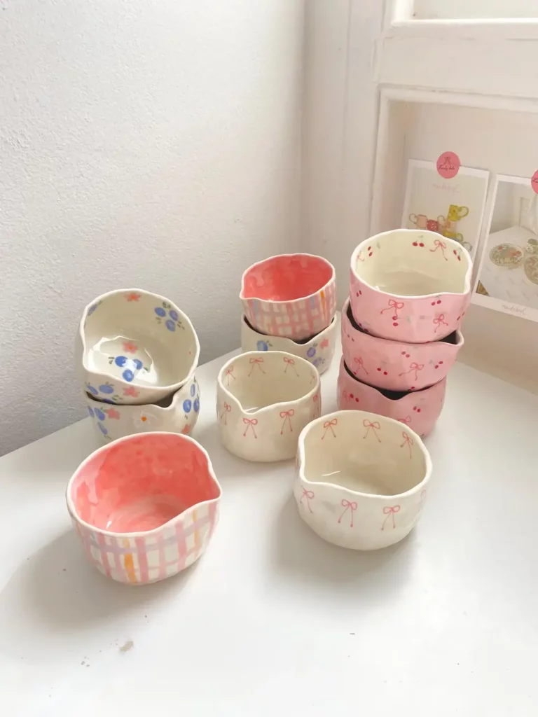 A collection of stacked ceramic matcha bowls with gingham, floral, and bow prints set on top of a white table.